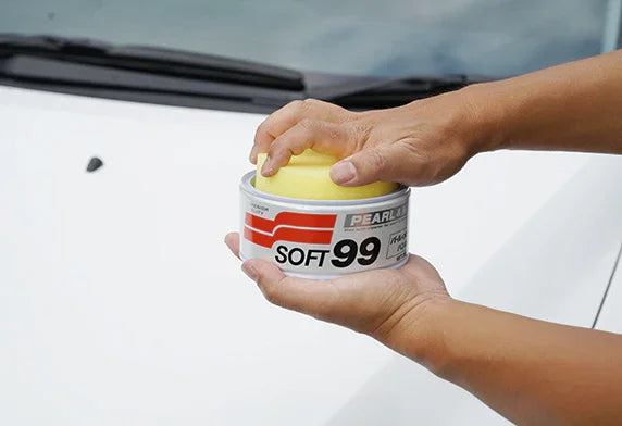 Hands holding Soft99 Fusso Coat wax tin with applicator sponge on car roof
