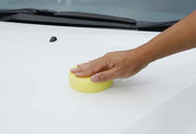Applying wax with sponge on white car bonnet surface
