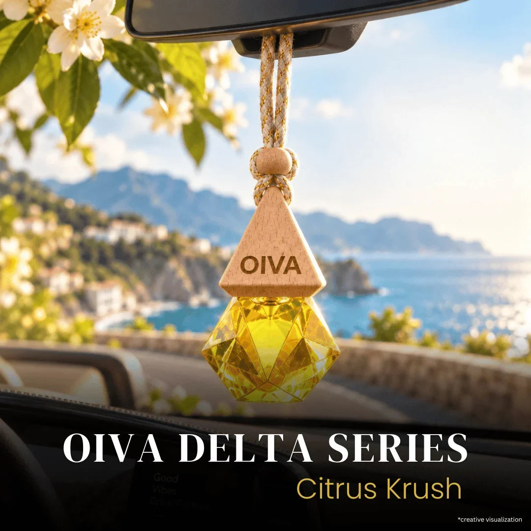 Oiva Delta Series Citrus Krush car air freshener hanging in a car window with a scenic coastal background. The product features a triangular wooden top engraved with 'OIVA' and a faceted yellow-green crystal lower section.